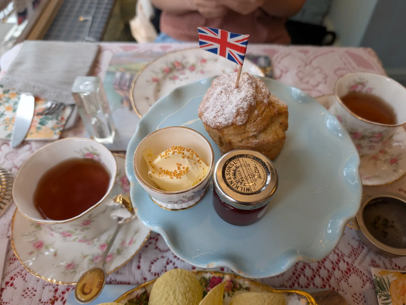 A traditional English cream tea: a scone with clotted cream and jam, served with pots of tea on vintage china.